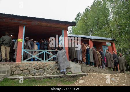 Srinagar, India. 13 maggio 2024. La gente aspetta in coda per esprimere il proprio voto al di fuori di un seggio elettorale durante la quarta fase del Lok Sabha, o camera bassa, delle elezioni parlamentari indiane in un villaggio collinare a Budgam, un'area nel distretto di Budgam della circoscrizione parlamentare di Srinagar. (Foto di Faisal Bashir/SOPA Images/Sipa USA) credito: SIPA USA/Alamy Live News Foto Stock