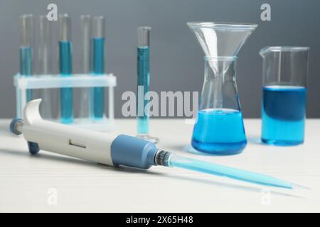 Analisi di laboratorio. Micropipetta e vetreria diversa con liquidi su tavolo in legno bianco, primo piano Foto Stock