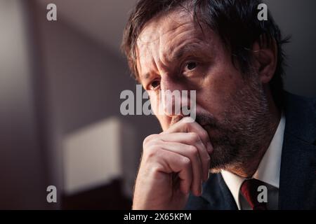 Un uomo d'affari che ripensa, ritratto alla testa di un imprenditore maschio medio adulto che pensa con la mano sul mento, attenzione selettiva Foto Stock