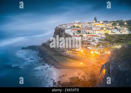 Ora blu sopra il villaggio sulla scogliera di Azenhas do Mar e le onde che si infrangono Foto Stock