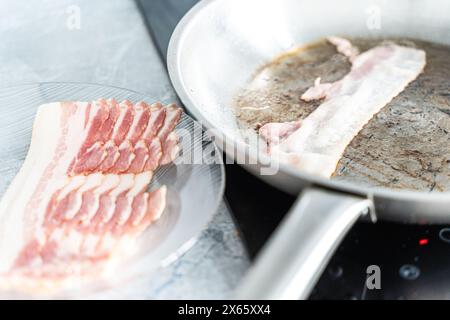 Per preparare la colazione, viene fritta la pancetta cruda su un piatto e una striscia di pancetta in una padella. Foto di alta qualità Foto Stock