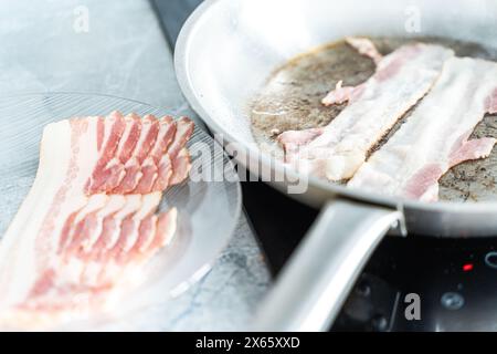 Per preparare la colazione, viene fritta la pancetta cruda su un piatto e una striscia di pancetta in una padella. Foto di alta qualità Foto Stock