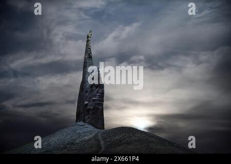 Una guglia solitaria illuminata di notte durante un luminoso sorgere di luna. Foto Stock