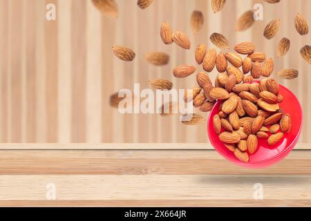 Le mandorle cadono in una ciotola rossa su un tavolo di legno. Concetto di cibo sano. Copia spazio. Foto Stock