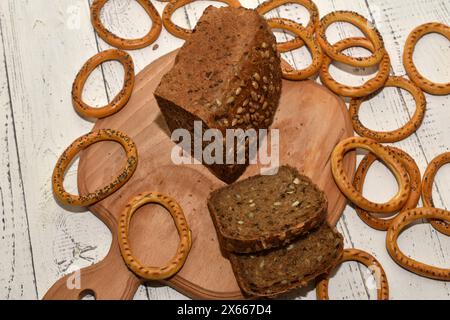 Una pagnotta di pane a base di farina di segale, cosparsa di semi di girasole, nonché pezzi e bagel tagliati da essa giacciono su un tagliere. Foto Stock