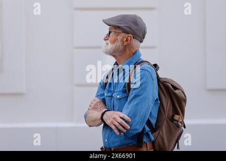 Ritratto di un bel anziano in città. Anziano uomo indipendente con zaino in visita a nuova città. Viaggi e viaggi da soli in pensione. Foto Stock