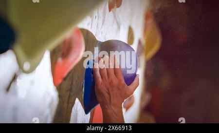 Forte scalatore esperto che pratica l'arrampicata in solitaria sul muro di Boulder in palestra. Uomo che fa esercizio presso la palestra Indoor fitness Facility, praticando sport estremi per il suo sano allenamento Lifestyle. Primo piano verticale Foto Stock