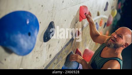 Forte scalatore esperto che pratica l'arrampicata in solitaria sul muro di Boulder in palestra. Uomo che fa esercizio presso la palestra Indoor fitness Facility, praticando sport estremi per il suo sano allenamento Lifestyle. Primo piano verticale Foto Stock