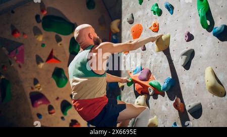 Forte scalatore esperto che pratica l'arrampicata in solitaria sul muro di Boulder in palestra. Uomo che fa esercizio presso la palestra Indoor fitness Facility, facendo sport estremi per il suo allenamento sano. Stile di vita Ritratto. Foto Stock