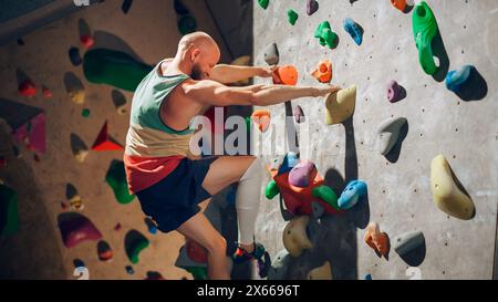 Forte scalatore esperto che pratica l'arrampicata in solitaria sul muro di Boulder in palestra. Uomo che fa esercizio presso la palestra Indoor fitness Facility, facendo sport estremi per il suo allenamento sano. Stile di vita Ritratto. Foto Stock