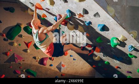 Forte scalatore esperto che pratica l'arrampicata in solitaria sul muro di Boulder in palestra. Uomo che fa esercizio presso la palestra Indoor fitness Facility, facendo sport estremi per il suo allenamento sano. Stile di vita Ritratto. Foto Stock