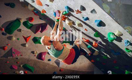 Forte scalatore esperto che pratica l'arrampicata in solitaria sul muro di Boulder in palestra. Uomo che fa esercizio presso la palestra Indoor fitness Facility, facendo sport estremi per il suo allenamento sano. Stile di vita Ritratto. Foto Stock