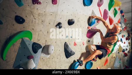 Forte scalatore esperto che pratica l'arrampicata in solitaria sul muro di Boulder in palestra. Uomo che fa esercizio presso la palestra Indoor fitness Facility, praticando sport estremi per il suo sano allenamento Lifestyle. Foto Stock