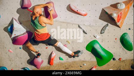 Forte esperto arrampicatore che pratica arrampicata in solitaria sul muro di Bouldering in una palestra. Uomo che fa esercizio presso la palestra Indoor fitness Facility, praticando sport estremi per il suo sano allenamento Lifestyle. Sparato da dietro. Foto Stock