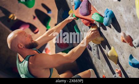 Forte scalatore esperto che pratica l'arrampicata in solitaria sul muro di Boulder in palestra. Uomo che fa esercizio presso la palestra Indoor fitness Facility, praticando sport estremi per il suo sano allenamento Lifestyle. Primo piano verticale Foto Stock