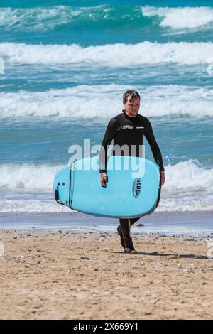 Un surfista che cammina fuori dal mare portando la sua tavola da surf a Fistral Beach a Newquay, in Cornovaglia, nel Regno Unito. Foto Stock