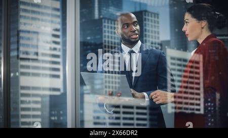 Ritratto di un CEO aziendale e Investment Manager di successo che parla, utilizzando un computer portatile mentre si trova in un ufficio cittadino. Due uomini d'affari di successo si sono confrontati con il software e-Commerce. Colpo esterno Foto Stock