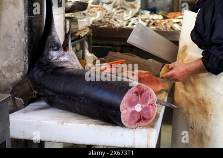 Dettaglio della mano di un pescivendolo che taglia spadaccino al pesce fresco di Ortigia Siracusa, storico mercato ittico italiano Foto Stock