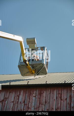 Riparazione di un tetto piatto di un edificio agricolo con ascensore giallo in una soleggiata giornata estiva a Skaraborg in Svezia Foto Stock