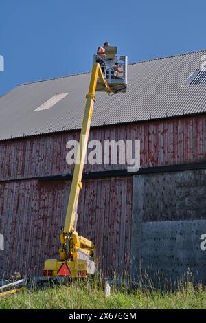 Riparazione di un tetto piatto di un edificio agricolo con ascensore giallo in una soleggiata giornata estiva a Skaraborg in Svezia Foto Stock