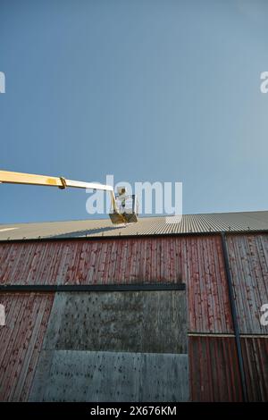 Riparazione di un tetto piatto di un edificio agricolo con ascensore giallo in una soleggiata giornata estiva a Skaraborg in Svezia Foto Stock