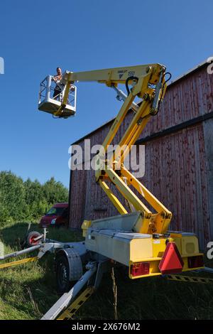 Riparazione di un tetto piatto di un edificio agricolo con ascensore giallo in una soleggiata giornata estiva a Skaraborg in Svezia Foto Stock