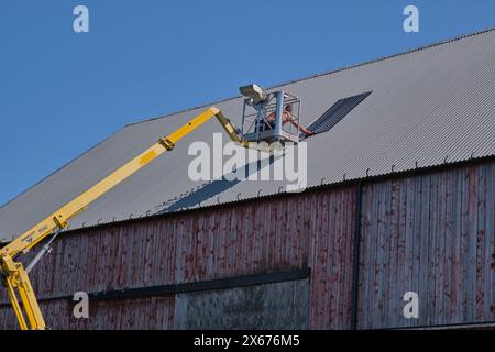 Riparazione di un tetto piatto di un edificio agricolo con ascensore giallo in una soleggiata giornata estiva a Skaraborg in Svezia Foto Stock