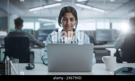 Ufficio diversificato: Ritratto di un bellissimo programmatore IT indiano che lavora su un computer desktop, sorridente. Ingegnere del software femminile che crea app, programma, videogame innovativi Foto Stock