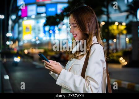 la donna si trova sul lato di una strada di notte, tenendo il cellulare e cercando di cavalcare Foto Stock