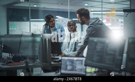 Gruppo diversificato di professionisti che si incontrano in Modern Office: Brainstorming i programmatori IT usano il computer insieme, parlano di strategia, discutono di pianificazione. I tecnici del software sviluppano un programma applicativo ispirativo Foto Stock