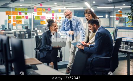 Nell'ufficio moderno: Diversi team di manager utilizzano computer portatili e tablet durante una riunione aziendale che discute di progetti aziendali. I dipendenti giovani, motivati ed esperti possono fare il brainstorming nella sala conferenze. Foto Stock