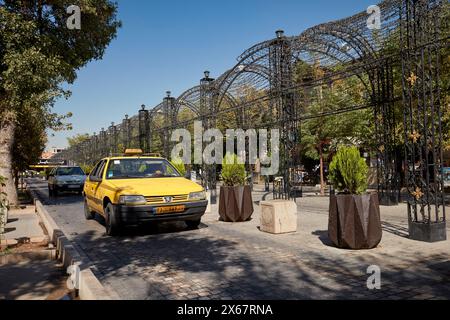 Un taxi giallo guida in una strada stretta costeggiata da alberi verdi nel centro storico di Shiraz, Iran. Foto Stock