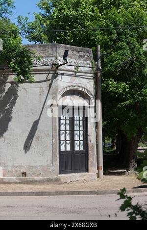 Un piccolo edificio con una porta nera e tende bianche. L'edificio e' circondato da alberi e ha un'ombra su di esso Foto Stock