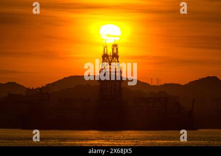 Impianto di trivellazione petrolifera nella baia di Guanabara con il sole che sorge sopra a Rio de Janeiro, Brasile Foto Stock