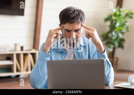 Uomo che si concentra intensamente mentre lavora su un notebook in ufficio domestico Foto Stock