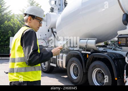 Lavoratore con tablet digitale accanto alla pompa per calcestruzzo montata su autocarro con miscelatore Foto Stock