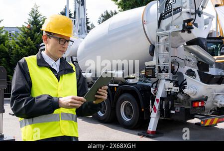 Lavoratore con tablet digitale accanto alla pompa per calcestruzzo montata su autocarro con miscelatore Foto Stock