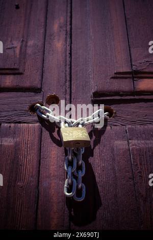 Vecchia porta in legno chiusa con una catena metallica spessa e un lucchetto Foto Stock