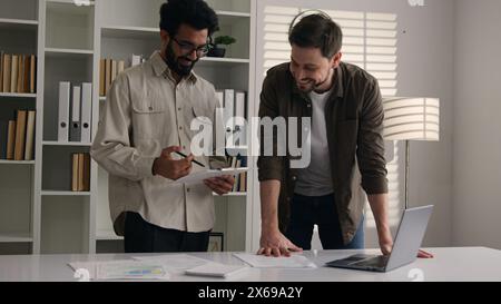 Due felici e sorridenti colleghi multietnici uomini d'affari partner in ufficio discutono progetto computer lavoro uomini indiani caucasici uomini uomini uomini uomini Foto Stock