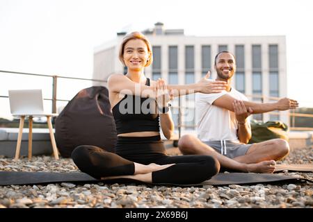 Uomo e donna seduti su tappeti con gambe incrociate e braccia allungate Foto Stock