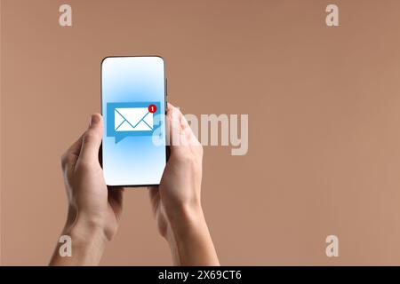 Notifica di un nuovo messaggio. Uomo con cellulare su sfondo beige scuro, primo piano Foto Stock