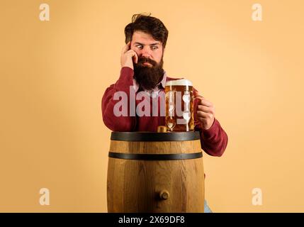 L'ora della birra. Sorprese l'uomo barbuto con birra alla spina su botte di legno. Elegante ragazzo con tazza di birra artigianale al ristorante, pub o bar. Vacanze Foto Stock