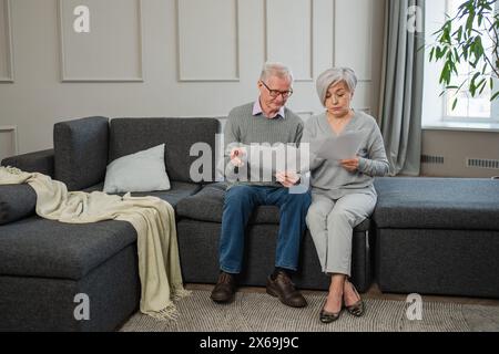 Triste stanco, deluso, coppia di anziani di mezza età siedono con un documento cartaceo. Infelice anziano maturo donna che legge banconote che gestiscono le finanze bancarie calcolano le tasse pianificazione prestito pagamento pensione Foto Stock