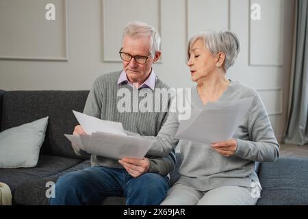 Triste stanco, deluso, coppia di anziani di mezza età siedono con un documento cartaceo. Infelice anziano maturo donna che legge banconote che gestiscono le finanze bancarie calcolano le tasse pianificazione prestito pagamento pensione Foto Stock