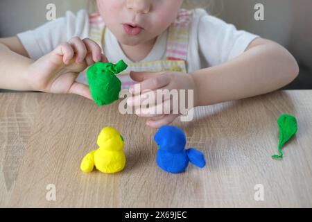 giocattoli in plastica per primi piani nelle mani di bimbi piccoli, bimbi piccoli, bionda di 2 anni scolpisce figure di personaggi di impasto colorato, concetto di fine m Foto Stock