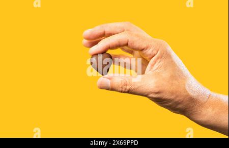 Mano di un uomo irriconoscibile isolata su sfondo giallo che regge un cioccolato a forma di cuore. Concetto d'amore al cioccolato Foto Stock