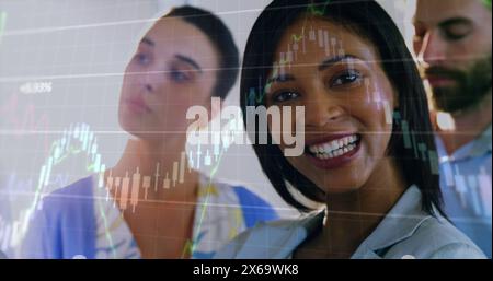 Immagine di grafici che si spostano su una donna d'affari birazziale sorridente con colleghi in ufficio Foto Stock