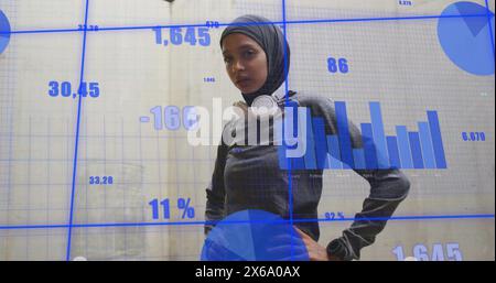 Giovane professionista birazziale che indossa hijab davanti a grafici digitali Foto Stock