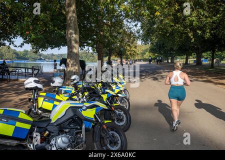 Hyde Park London, motociclette della polizia metropolitana parcheggiate all'esterno del caffè al Serpentine mentre una donna bionda fa jogging e passa oltre, Inghilterra, Regno Unito, 2023 Foto Stock