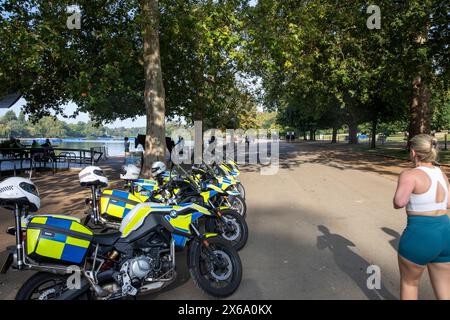 Hyde Park London, motociclette della polizia metropolitana parcheggiate all'esterno del caffè al Serpentine mentre una donna bionda fa jogging e passa oltre, Inghilterra, Regno Unito, 2023 Foto Stock